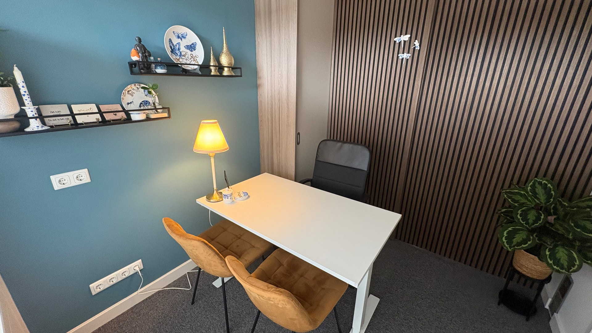 Praktijkruimte van de ReAttach praktijk in Vlijmen met blauwgroene wand, bureau en grote plant